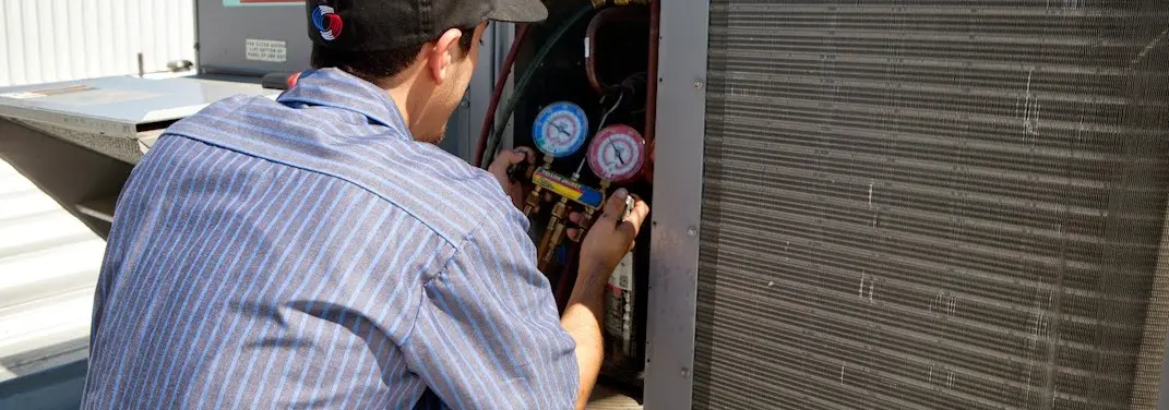 HVAC technician servicing a condenser unit in Monroe